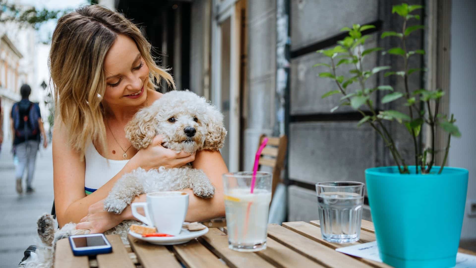 Woman cuddling dog at outdoor cafe table.